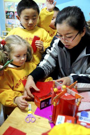 A foreign girl learns to make lantern in Zhongsheng Kindergarten in Lianyungang, a port city of east China's Jiangsu Province, Dec. 29, 2009. An activity of raising children's environmental protection awareness was held here on Tuesday during which children from home and abroad made varied New Year lanterns from waste articles. [Xinhua]