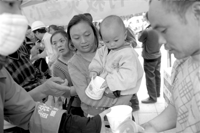 昨天，第一批救灾奶粉送抵芦山，家长抱着孩子在芦山县医院门口排队领取。
