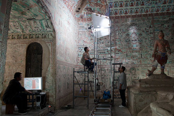 A photography team captures images of ancient murals in a cave of Dunhuang Mogao Grottoes, in Gansu province. Provided to China Daily