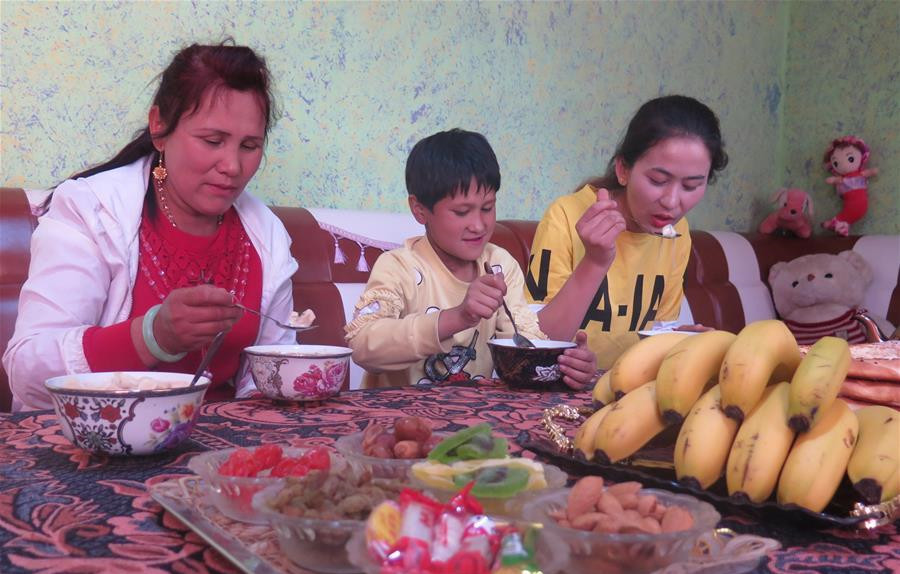 在新疆疏勒县巴合齐乡巴合齐村，麦尔哈巴·乌拉伊木（右）和母亲（左）、妹妹在富民安居房中享用午餐