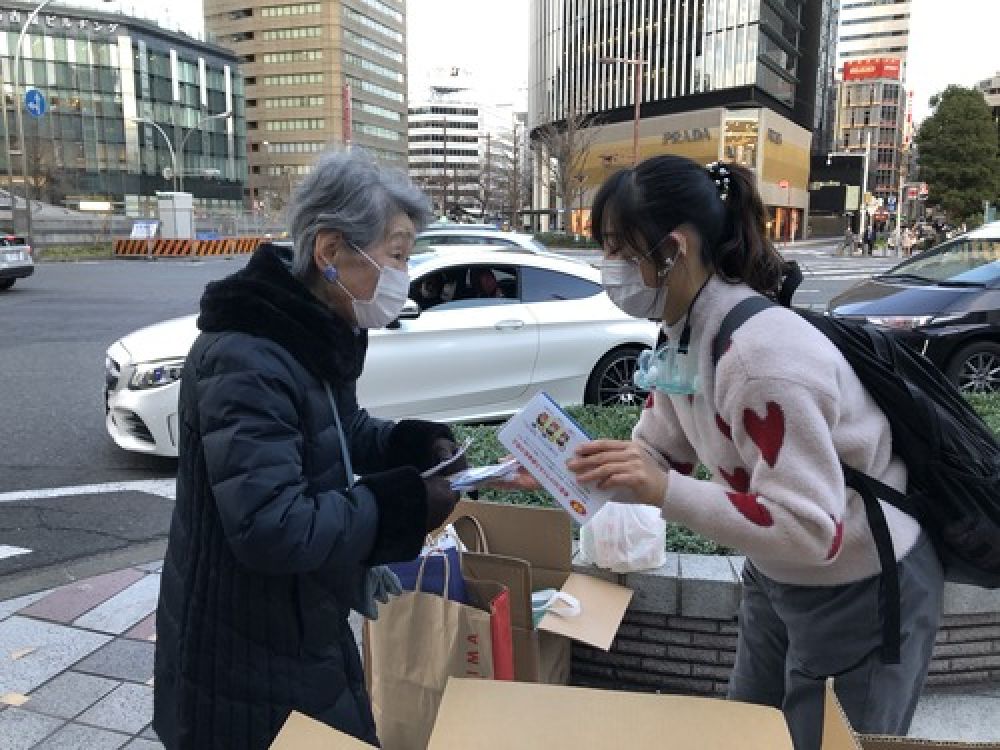 2月20日，在日本名古屋，一名在日华侨华人志愿者团体成员（右）给一名老人发放口罩。新华社发