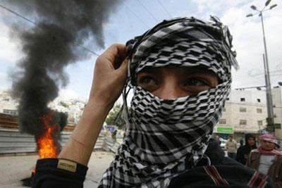 A masked Palestinian demonstrator stands near burning tires during clashes with Israeli forces in the West Bank city of Hebron. (AFP/Hazem Bader)