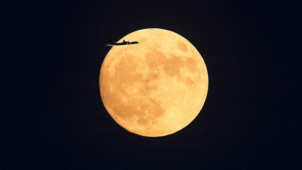 Airplane flies in front of full moon in Toronto