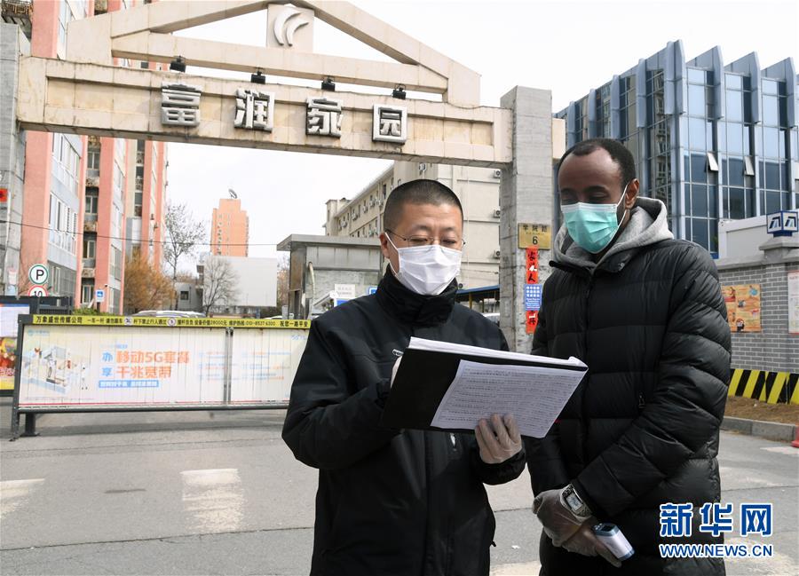 3月12日，在北京市海淀区学院路街道富润家园社区出入口，外籍志愿者阿里（右）与社区工作人员交流。 新华社记者 任超 摄