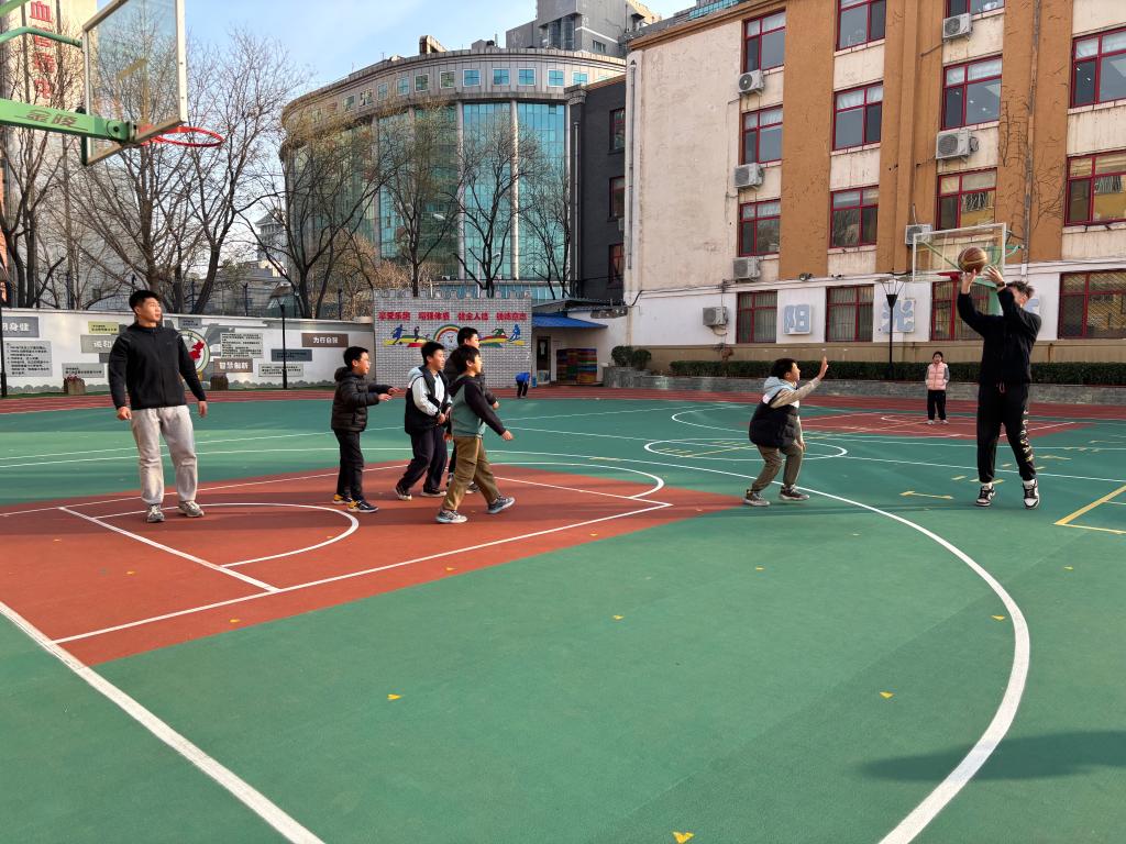 在北京市西城区奋斗小学，体育教师与学生一起打篮球。